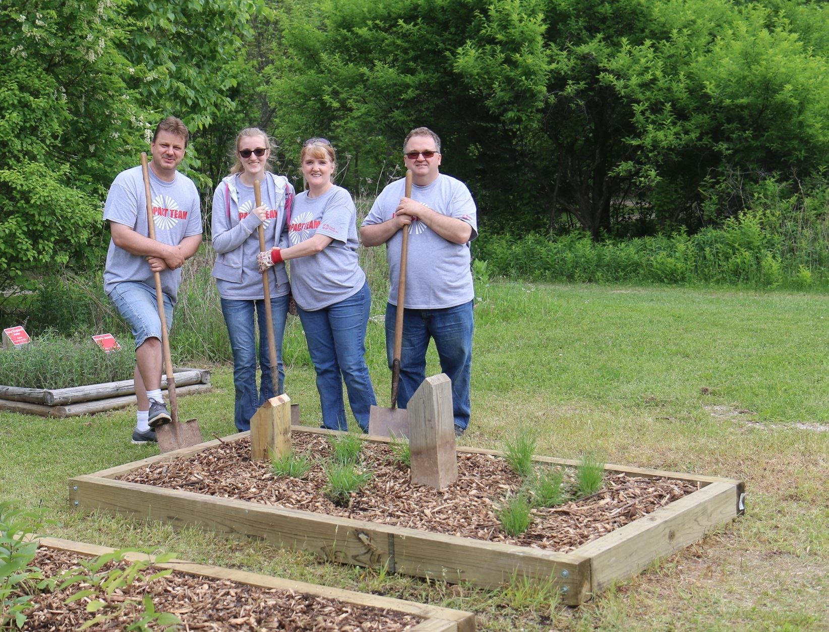 Two men and two women holding shovels. They are standing next to rectangular garden beds they just p